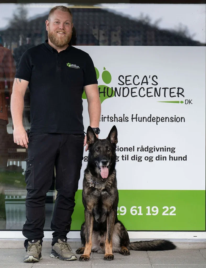Mand og hund foran Secas Hundecenter skilt